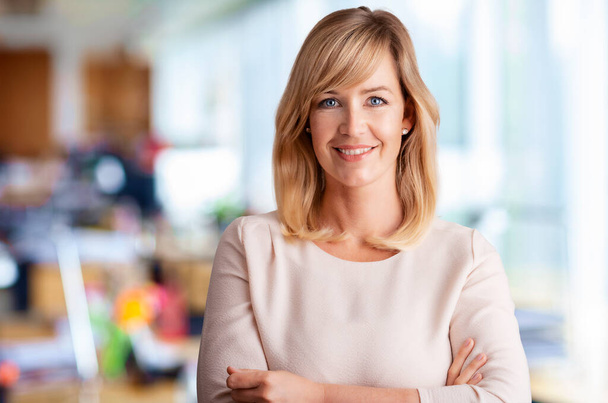 Portrait of smiling blond haired businesswoman while standing with arms crossed at the office. - Photo, Image