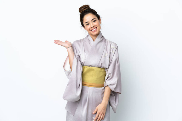Kobieta ubrana w kimono na odosobnionym tle, trzymająca na dłoni wyimaginowaną przestrzeń do wstawiania reklam. - Zdjęcie, obraz