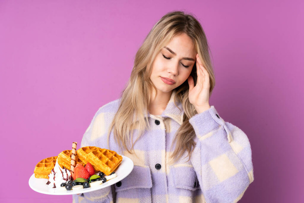 Teenager Russian girl holding waffles isolated on purple background with headache - Photo, Image