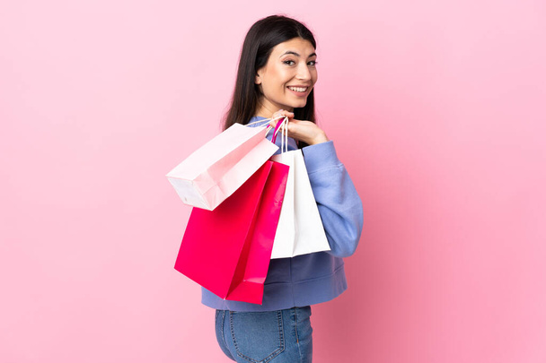 Nuori brunette tyttö yli eristetty vaaleanpunainen tausta tilalla ostoskassit ja hymyilevä - Valokuva, kuva