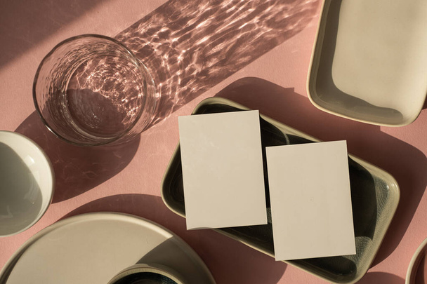 Пустая бумажная карточка с макетом копировального места на пыльном розовом фоне. Эстетическая богемная модель бизнес-бренда. Керамические плиты и стекло с яркими солнечными тенями - Фото, изображение