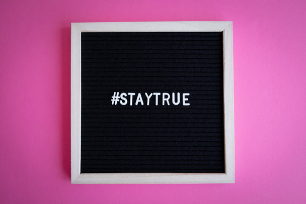 Een top view shot van een schoolbord met een wit frame met een "# staytrue" hashtag op een roze achtergrond - Foto, afbeelding