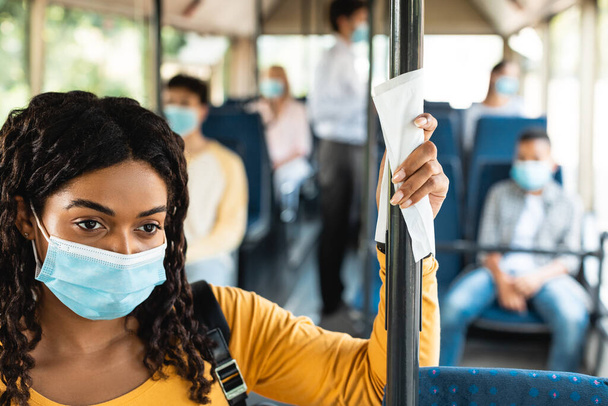 Yüz maskeli siyah bir kadın otobüste duruyor. - Fotoğraf, Görsel