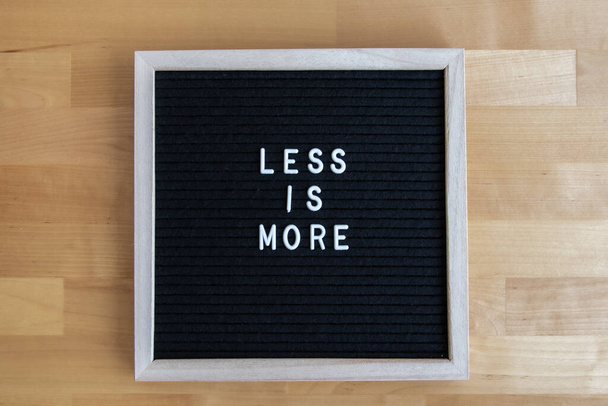 a top view shot of a blackboard with "less is more" quote on it at a wooden table - Φωτογραφία, εικόνα