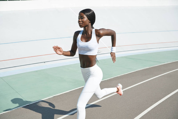 Beautiful young African woman in sports clothing running on track outdoors - Fotografie, Obrázek