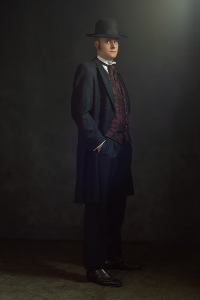 Young man in stylish vintage Victorian attire stands in a room in front of a dark gray wall. - Photo, Image