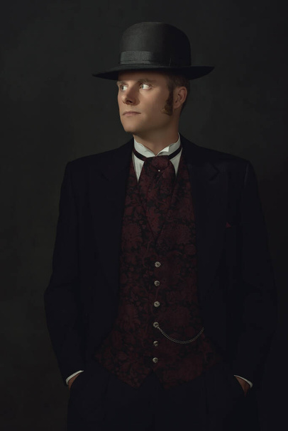 Shadowy retrato de un joven con estilo vintage traje victoriano en frente de una pared gris oscuro. - Foto, Imagen