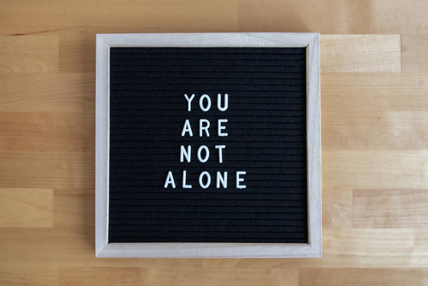 a top view shot of a blackboard with "you are not alone" quote on it at a wooden table - Foto, Imagen