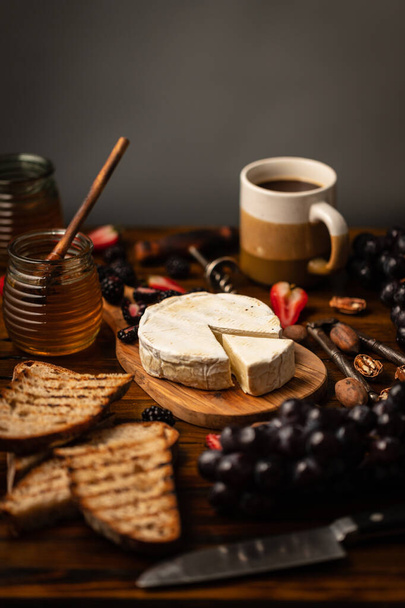 A vertical shot of a tiny white cake with grapes, honey, and coffee around it on a wooden table - Foto, imagen