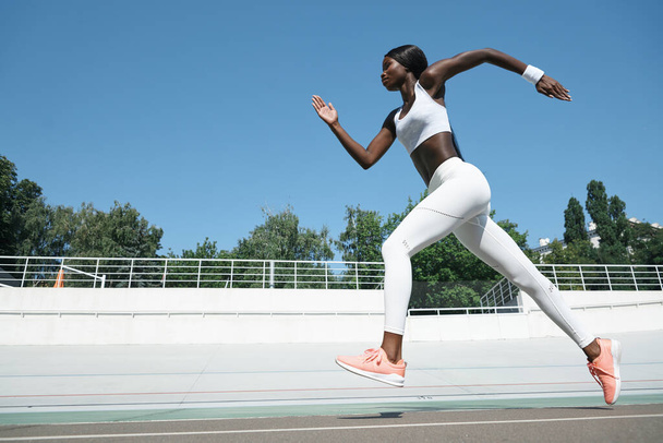 Confident young African woman in sports clothing running on track outdoors - Photo, Image