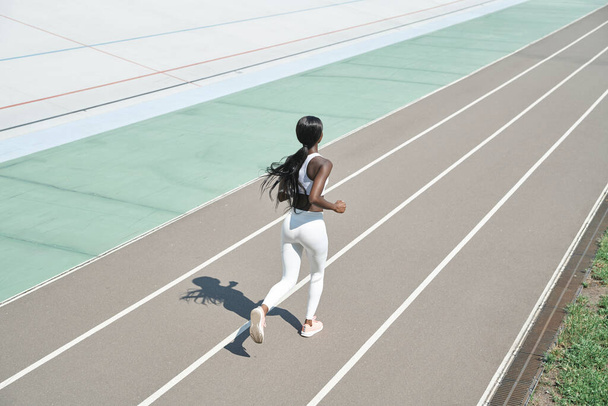 Draufsicht auf die schöne junge Afrikanerin in Sportkleidung, die im Freien auf der Strecke läuft - Foto, Bild