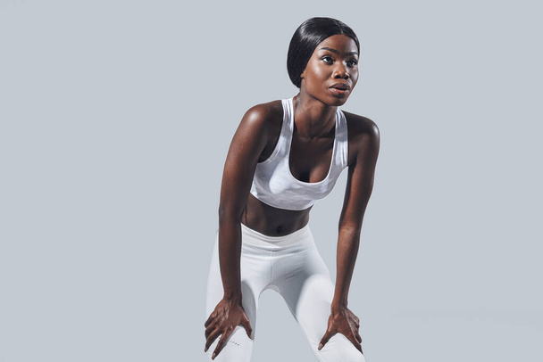Confident young African woman in sports clothing standing against gray background - Zdjęcie, obraz