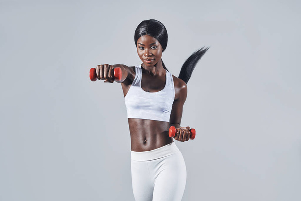 Beautiful young African woman in sports clothing exercising with dumbbells - Photo, image