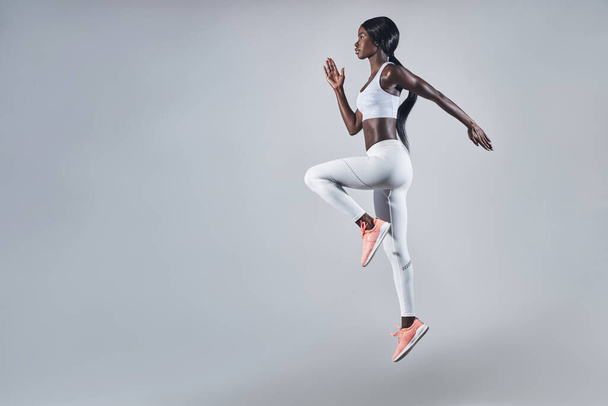 Full length of confident young African woman in sports clothing jumping against gray background - Photo, Image