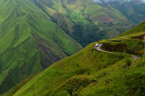 Ajoneuvo asfalttitiellä, joka sijaitsee vuorijonossa, jossa on vihreä kasvillisuus ja matalat puut. - Valokuva, kuva