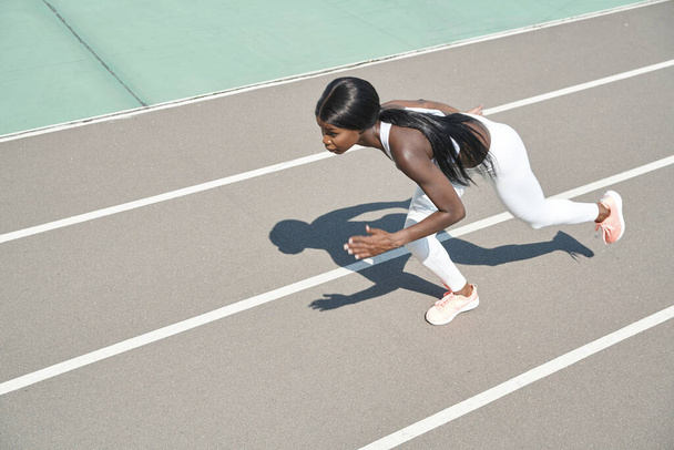 Top view of beautiful young African woman in sports clothing running on track outdoors - Foto, imagen