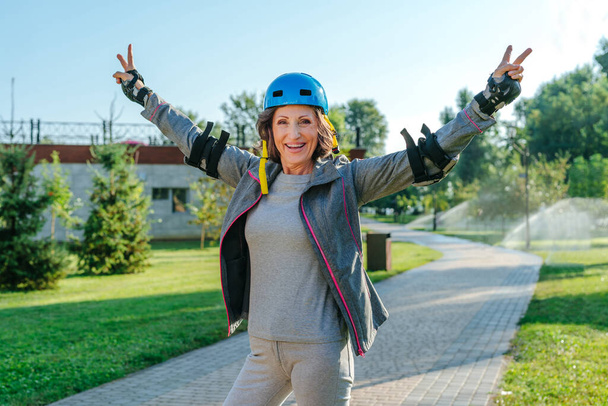 Happy mature woman rollerblading in the park wearing helmet, protective helmet, knee pads, elbow pads - Photo, Image