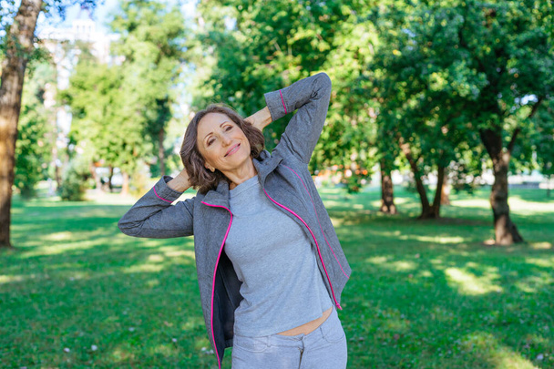 Szczęśliwa dojrzała kobieta w sportowej odzieży robi ćwiczenia w parku. - Zdjęcie, obraz