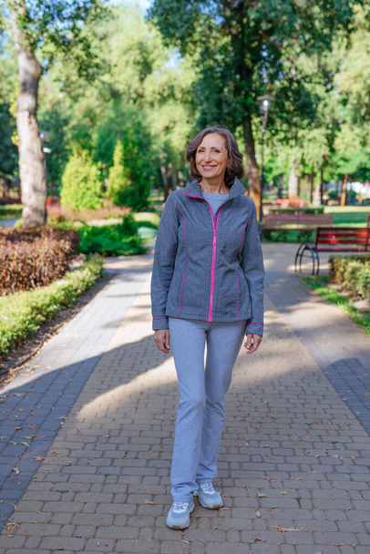 Boldog érett nő visel sport ruházat séta a parkban. - Fotó, kép