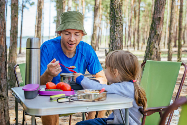 Joven padre con hija almorzando al aire libre. Vacaciones familiares. Camping en el bosque. - Foto, Imagen