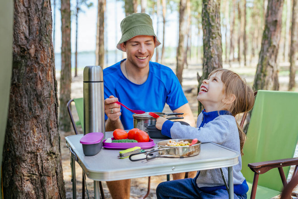 Young man father with daughter having lunch outdoor. Family holiday. Camping in the forest. - Photo, Image