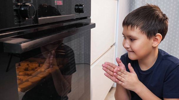 boy sits and looks into the oven while waiting for a cookie - Fotografie, Obrázek
