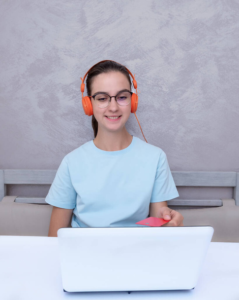 Caucasian student girl sitting at the table holding credit card using laptop to buy online learning course, vertical frame. Online shopping, e-commerce, online learning. - Φωτογραφία, εικόνα
