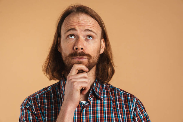 Bearded ginger man wearing plaid shirt thinking and looking upward isolated over beige background - Foto, immagini