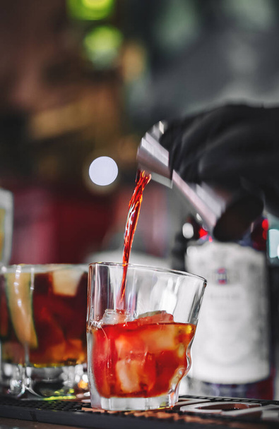 hands of a bartender with black gloves making cocktail on a bar counter. - Fotó, kép