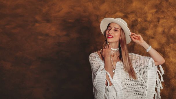 Portrait pretty happy stylish young woman with blonde hair in white clothes and hat on gold background looks at camera with satisfaction. Concept of an emotional portrait. Copy space for site - Foto, afbeelding