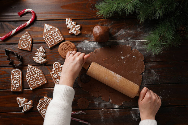 Μπισκότα με μελόψωμο και λευκή ζάχαρη σε σχήμα σπιτιού και ζύμη μελιού σοκολάτας τυλιγμένη σε ξύλινο τραπέζι περιτριγυρισμένη από χριστουγεννιάτικη διακόσμηση - Φωτογραφία, εικόνα