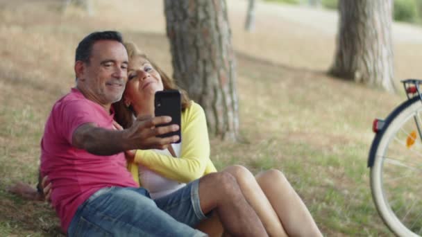Amoureux caucasiens assis sur la pelouse et de prendre une photo conjointe  - Séquence, vidéo