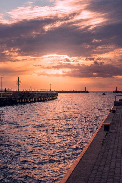 Largo rompeolas de hormigón junto a la entrada del puerto en Darlowko, Polonia iluminado por el sol poniente. Siluetas de los dos pequeños faros al final del puerto.  - Foto, imagen