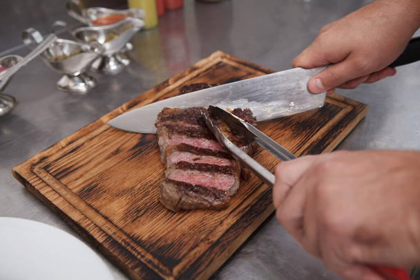 Шеф-кухар нарізає яловичий стейк на дерев'яній обробній дошці
 - Фото, зображення