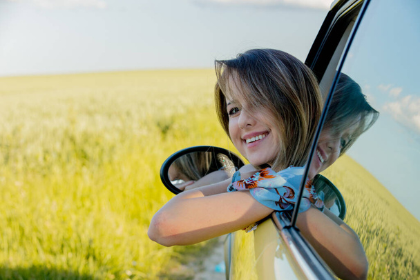 young girl in a car on green wheat field - Foto, afbeelding