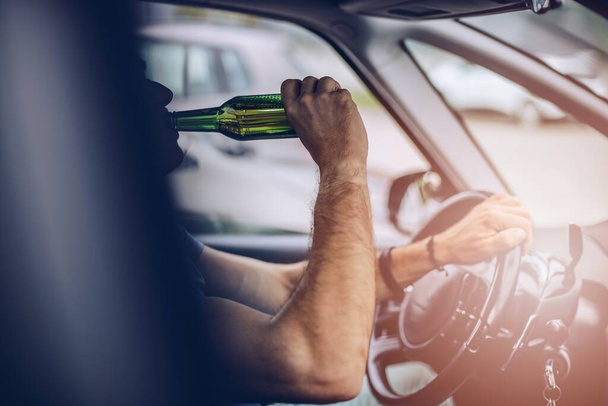 Człowiek pije piwo podczas jazdy samochodem. - Zdjęcie, obraz