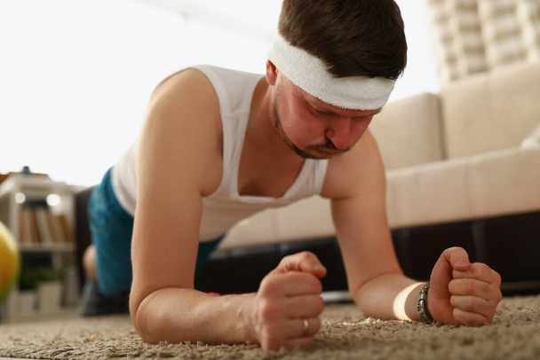 Мужчина выполняет упражнения на доске в квартире на ковре - Фото, изображение