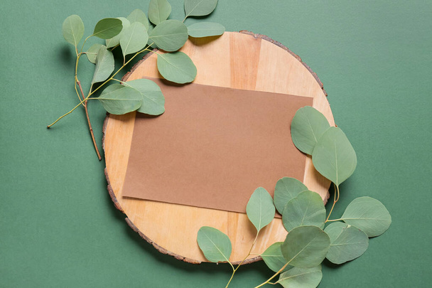 Σύνθεση με λευκή κάρτα, ξύλινη σανίδα και κλαδιά φυτών σε φόντο χρώματος - Φωτογραφία, εικόνα