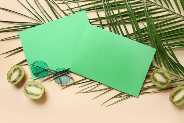 Összetétel üres kártyákkal, napszemüveggel, kivivel és pálmalevéllel színes háttéren - Fotó, kép