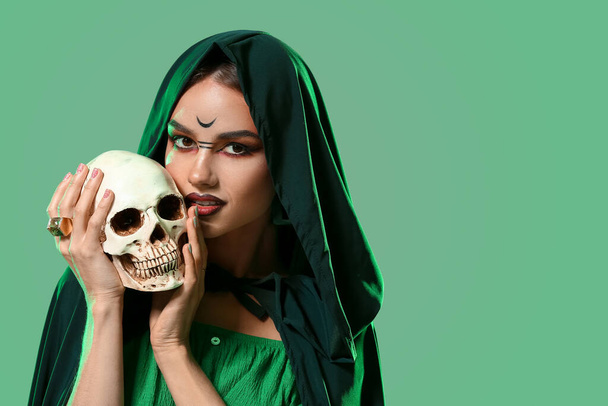 Joven bruja con cráneo sobre fondo de color - Foto, Imagen