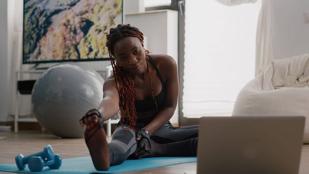 Mujer con piel negra haciendo ejercicio en sala de estar estirando ejercicio - Foto, Imagen