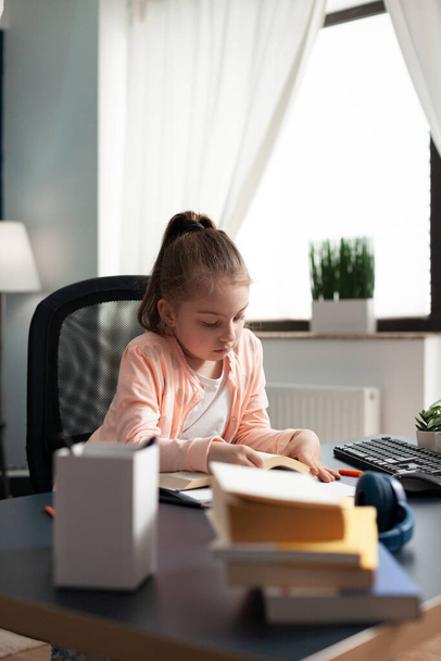 Kisiskolás lány jegyzetel és ír az íróasztalnál. - Fotó, kép