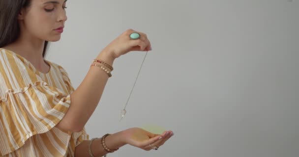 Young woman with pendulum on grey background - Footage, Video