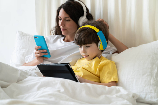 paresseux maman et enfant passé la matinée couché dans le lit faire du shopping en ligne dans le téléphone et jouer à des jeux sur tablette - Photo, image