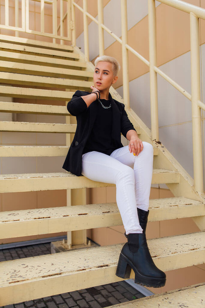 Young stylish business woman with short hair and nose piercing. Confident girl look like lesbian sitting on the stairs near business center - Foto, Bild