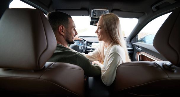 Feliz hombre y mujer viajando en coche. Vista trasera de la hermosa pareja joven sentada en los asientos delanteros del pasajero y sonriendo mientras el hombre guapo conduce el automóvil cómodo. - Foto, imagen