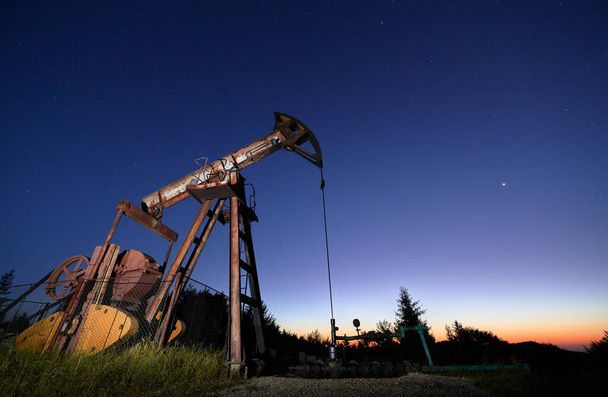 Piękny widok panoramiczny nocnego oleju złożonego z oleju ropopochodnego jack. Pompa oleju rocker-maszyna z fioletowym błękitnym niebem o wschodzie słońca na tle. Pojęcie przemysłu naftowego i wydobycia ropy naftowej. - Zdjęcie, obraz