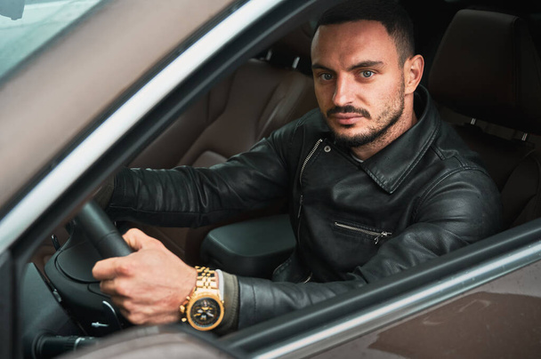 Portrait of handsome young man driving modern car. Guy driver wearing casual clothes and gold watch. - Φωτογραφία, εικόνα