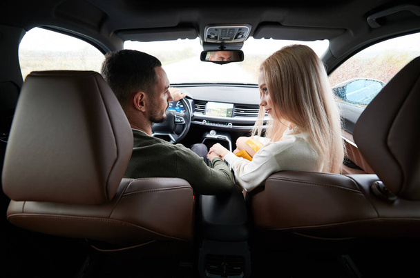 Šťastný muž a žena cestují v autě. Zadní pohled na krásný mladý pár sedí na předních sedadlech spolujezdce a usmívá se, zatímco hezký muž řídí pohodlný automobil. - Fotografie, Obrázek