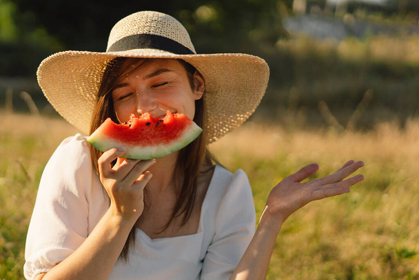 Szczęśliwa dziewczyna w parku z orzeźwiającym owocem arbuza. Kobieta je kawałek arbuza. - Zdjęcie, obraz